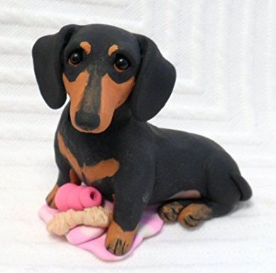 a toy dachshund is sitting on the floor with a pink object in it's mouth