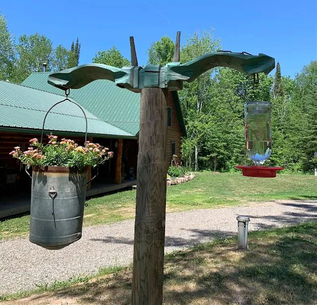 a large metal bucket with flowers hanging from it's side next to a wooden pole