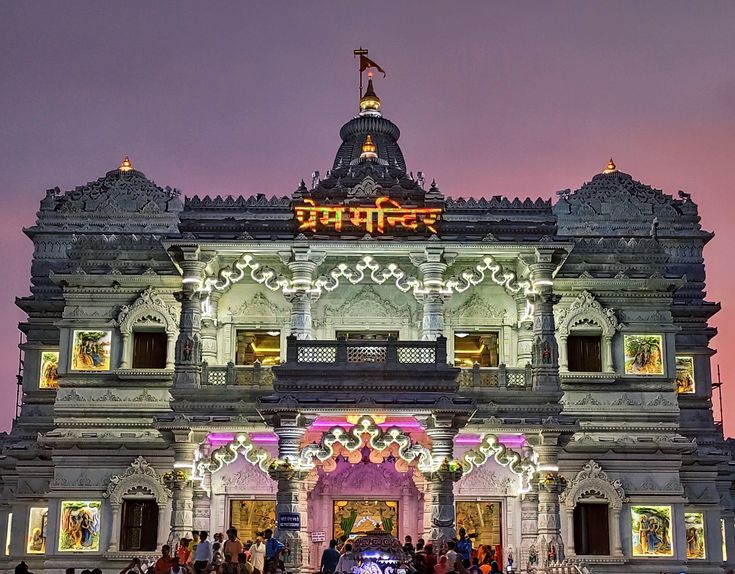 people are standing in front of an ornate building with lights and decorations on it at night