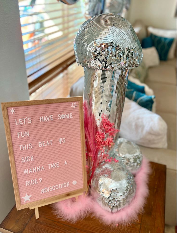 a pink sign sitting on top of a wooden table next to a silver vase filled with flowers