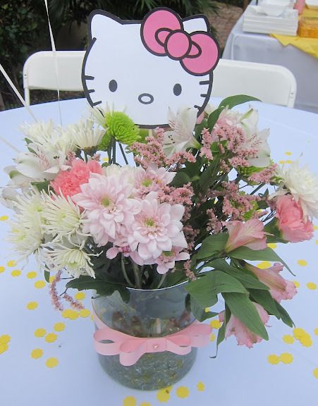 a vase filled with pink and white flowers on top of a table next to a sign that says hello kitty