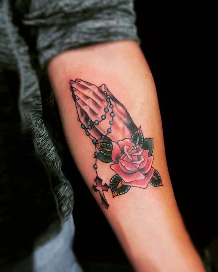 a woman's arm with a rose and praying hands tattoo on her left forearm