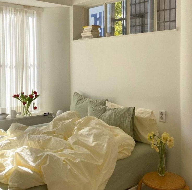 an unmade bed with white sheets and pillows in front of a window filled with flowers