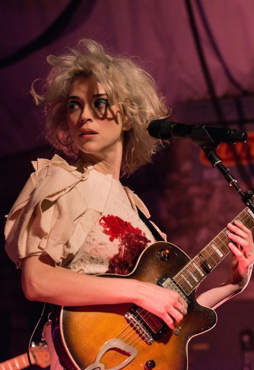 a woman holding a guitar while standing in front of a microphone