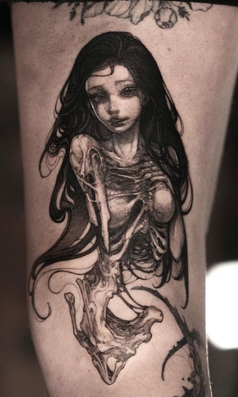 a woman's leg with a tattoo on it and a skeleton in the background