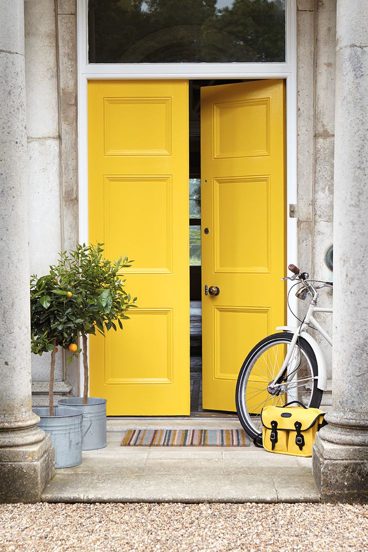 a bicycle parked in front of a yellow door with potted plants next to it