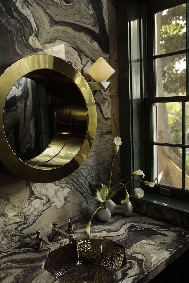 a bathroom with marble counter tops and gold accents on the wall, along with a round mirror