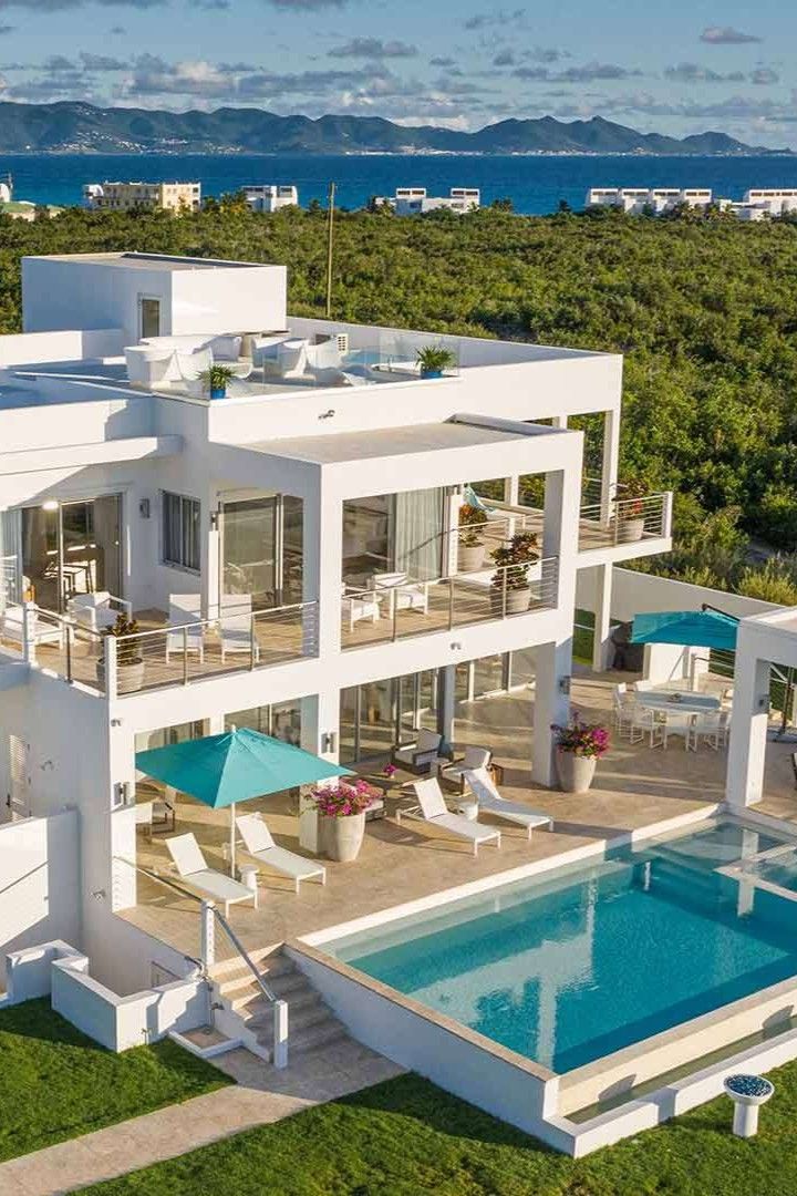 an aerial view of a large white house with pool and patio furniture in the foreground