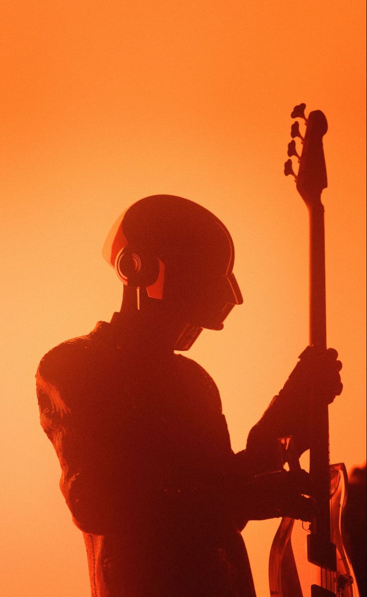 the silhouette of a man with a guitar in his hand, against an orange sky