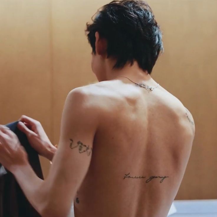 a man with no shirt is looking at his reflection in the mirror and has tattoos on his back