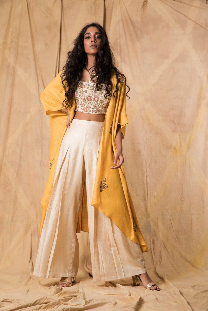 a woman standing in front of a backdrop wearing a yellow jacket and white pants with her hands on her hips