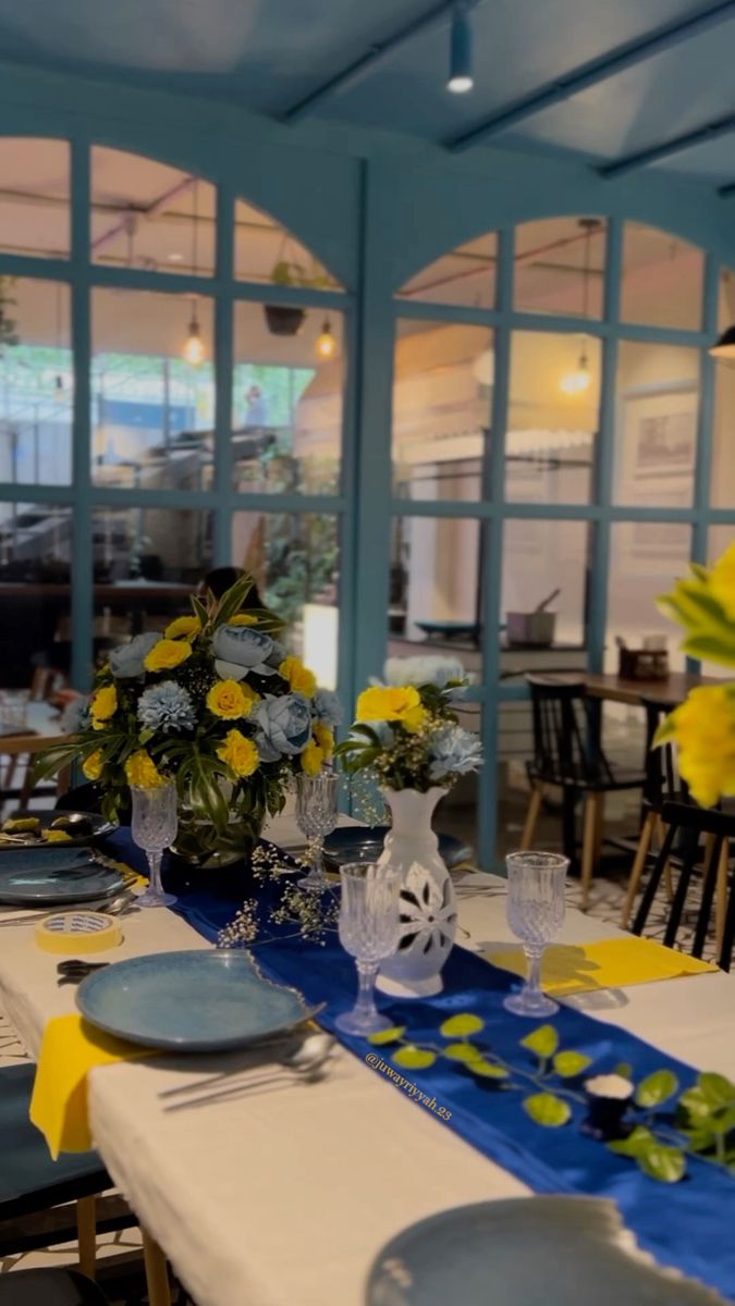 a dining room table set with blue and yellow flowers in vases on the tables