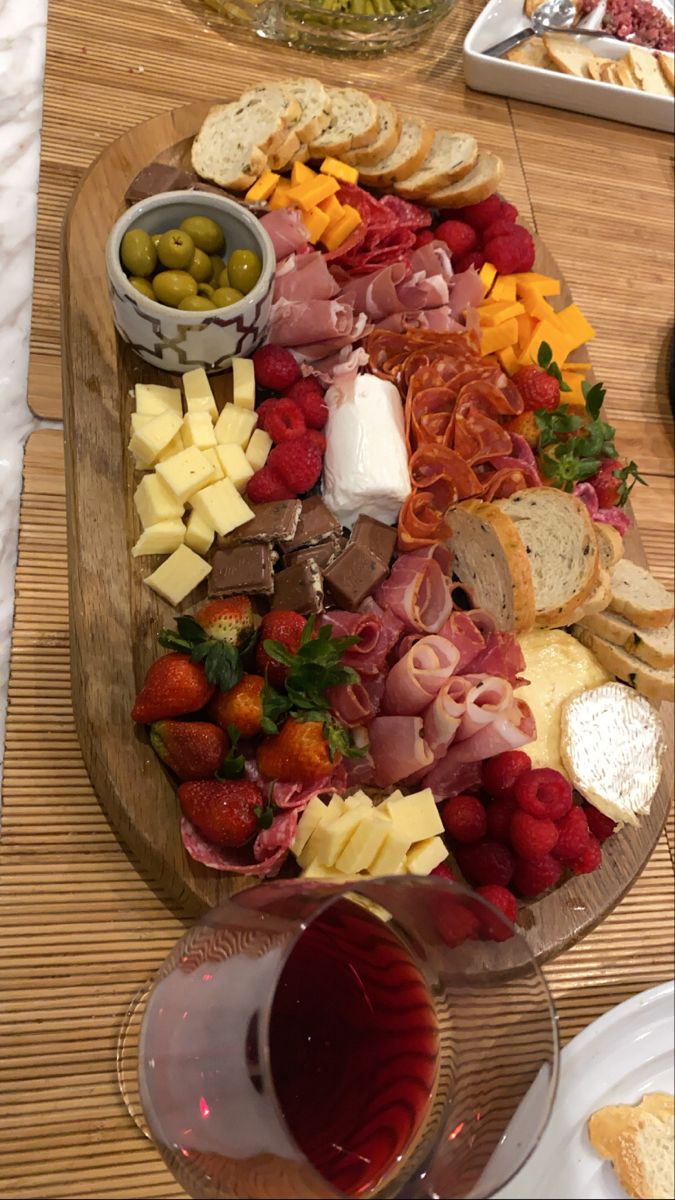 an assortment of cheeses, meats and fruit on a platter with wine