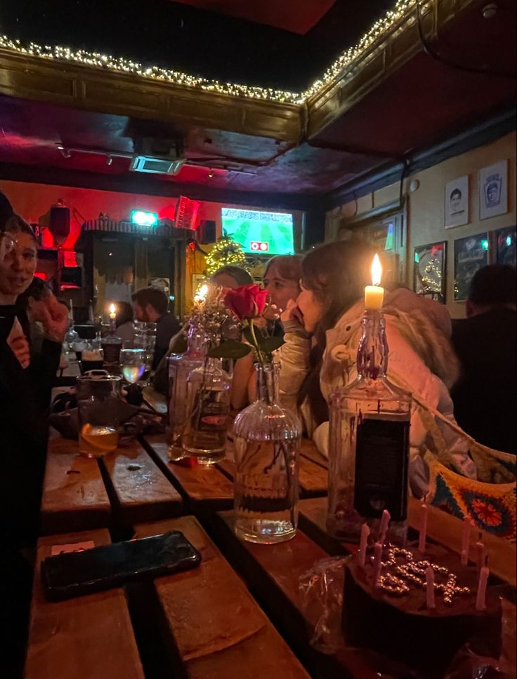 people sitting at a table with candles in front of them and one person holding a cell phone