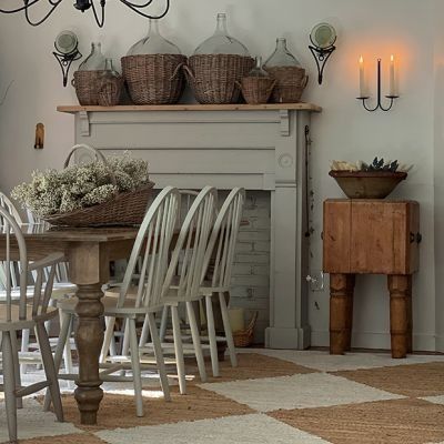 a dining room table and chairs in front of a fireplace with candles on the mantle