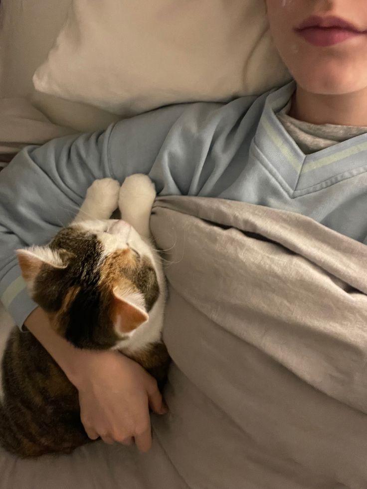 a person laying in bed with a cat on their lap and one arm wrapped around them