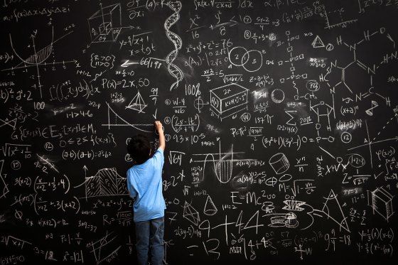 a young boy writing on a blackboard with lots of white chalk and some calculations