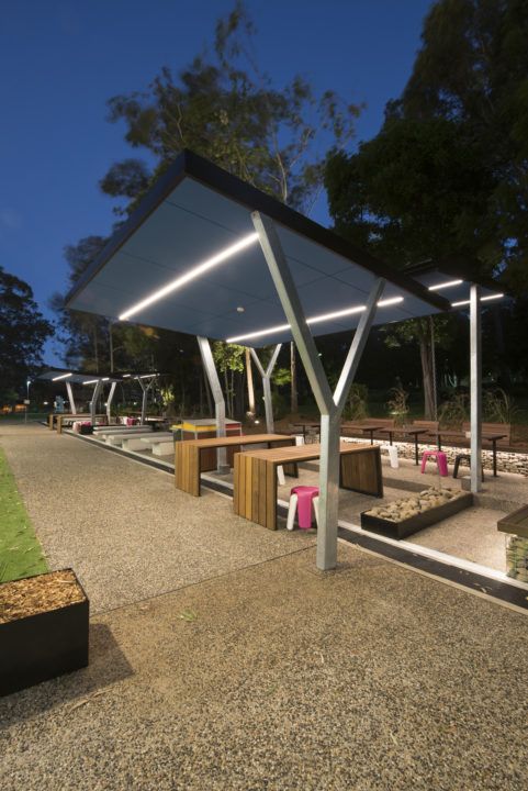 an outdoor seating area at night with benches and lights on the side walk in front of it