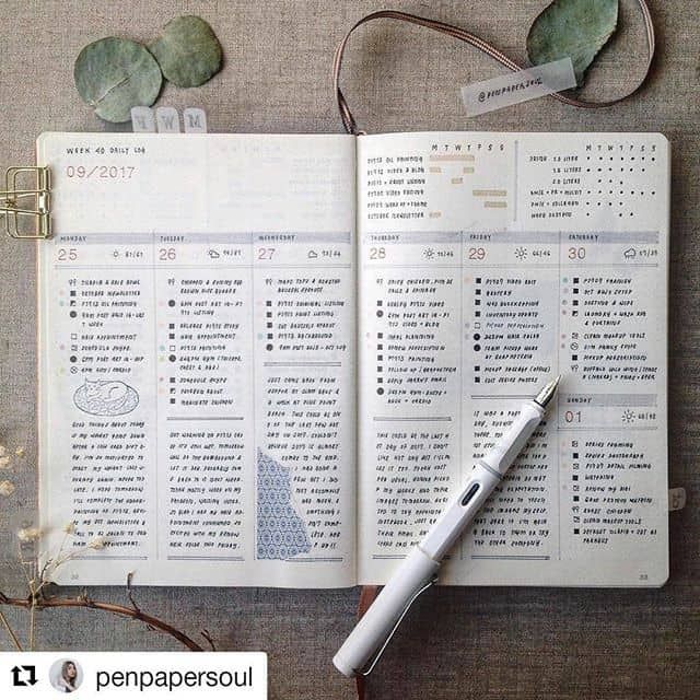 an open planner with a pen on top of it next to some plants and leaves