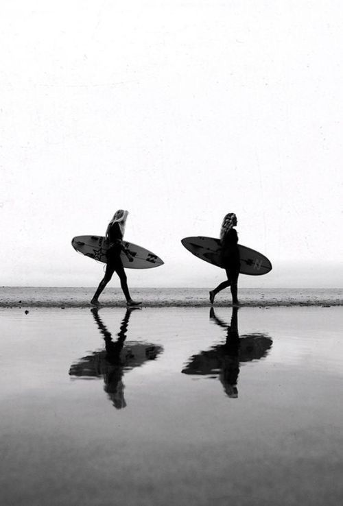 two people carrying surfboards walking on the beach in front of the ocean with their backs to the camera