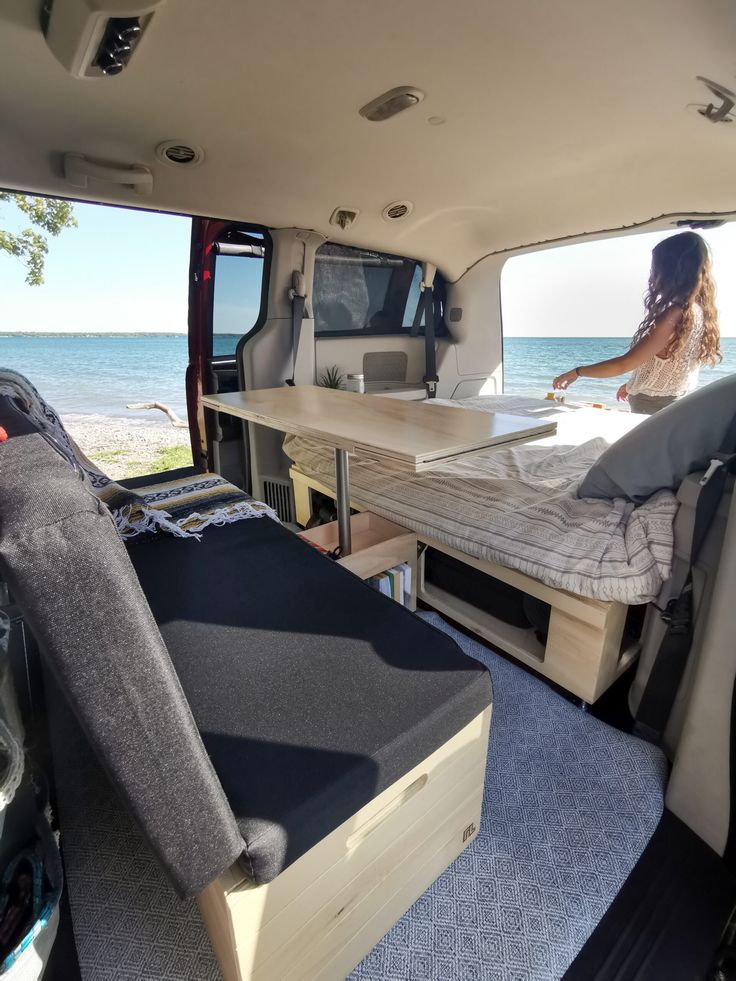 a woman sitting in the back of a van looking out at the ocean and beach