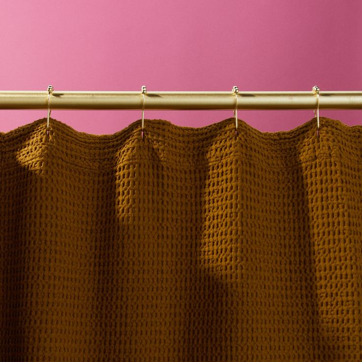 a close up of a curtain on a rod with pink wall in the back ground