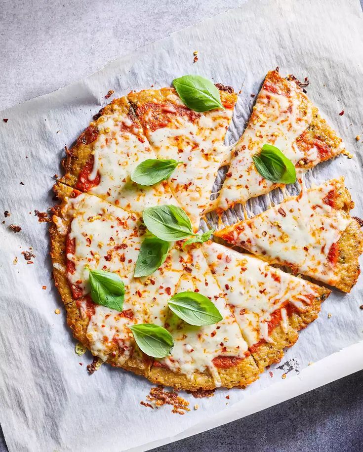 a pizza with cheese and basil on top is cut into four slices, sitting on a piece of parchment paper