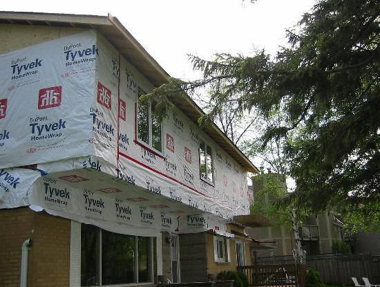 a house under construction with the roof covered in tarp and windows taped up to it's side