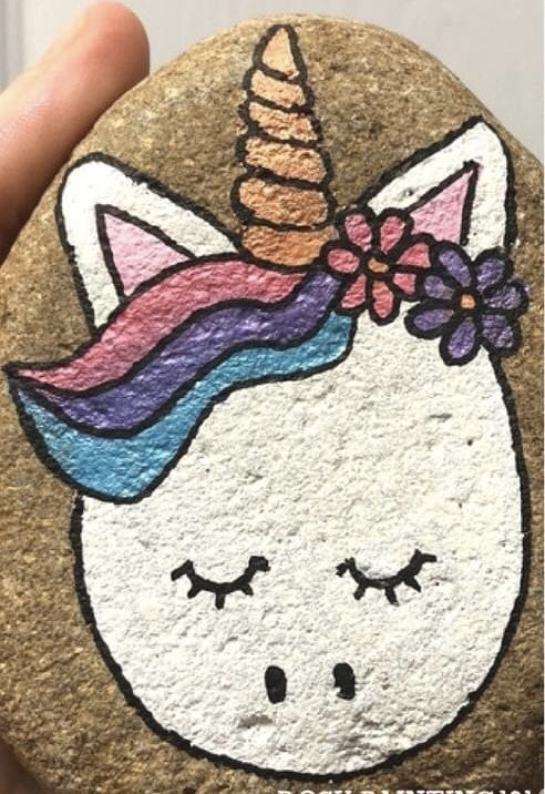 a hand holding a rock with a drawing of a unicorn on it's face