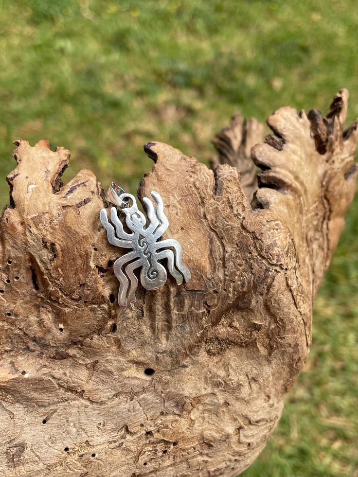 a small silver spider brooch sitting on top of a piece of wood