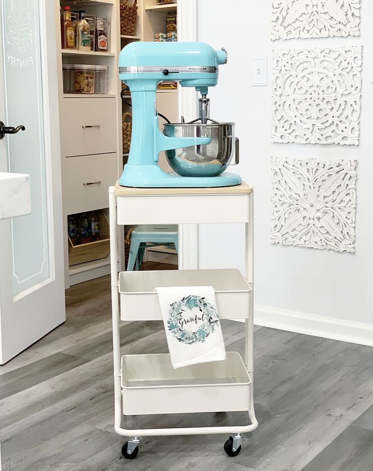 a blue mixer sitting on top of a cart next to a kitchen sink and cabinets