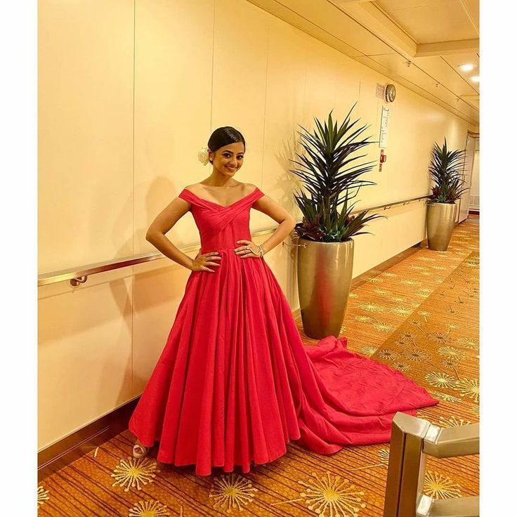 a woman in a red dress standing next to a plant