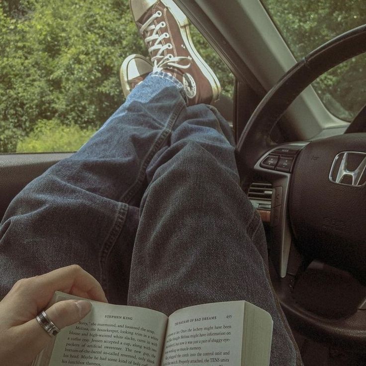 a person is sitting in the driver's seat with their feet up and reading a book