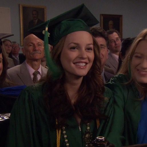 two women in graduation gowns smile at the camera while others look on from behind them