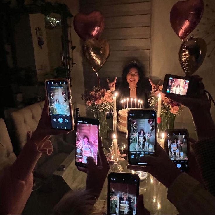 a group of people holding up their cell phones with candles in front of them and balloons behind them