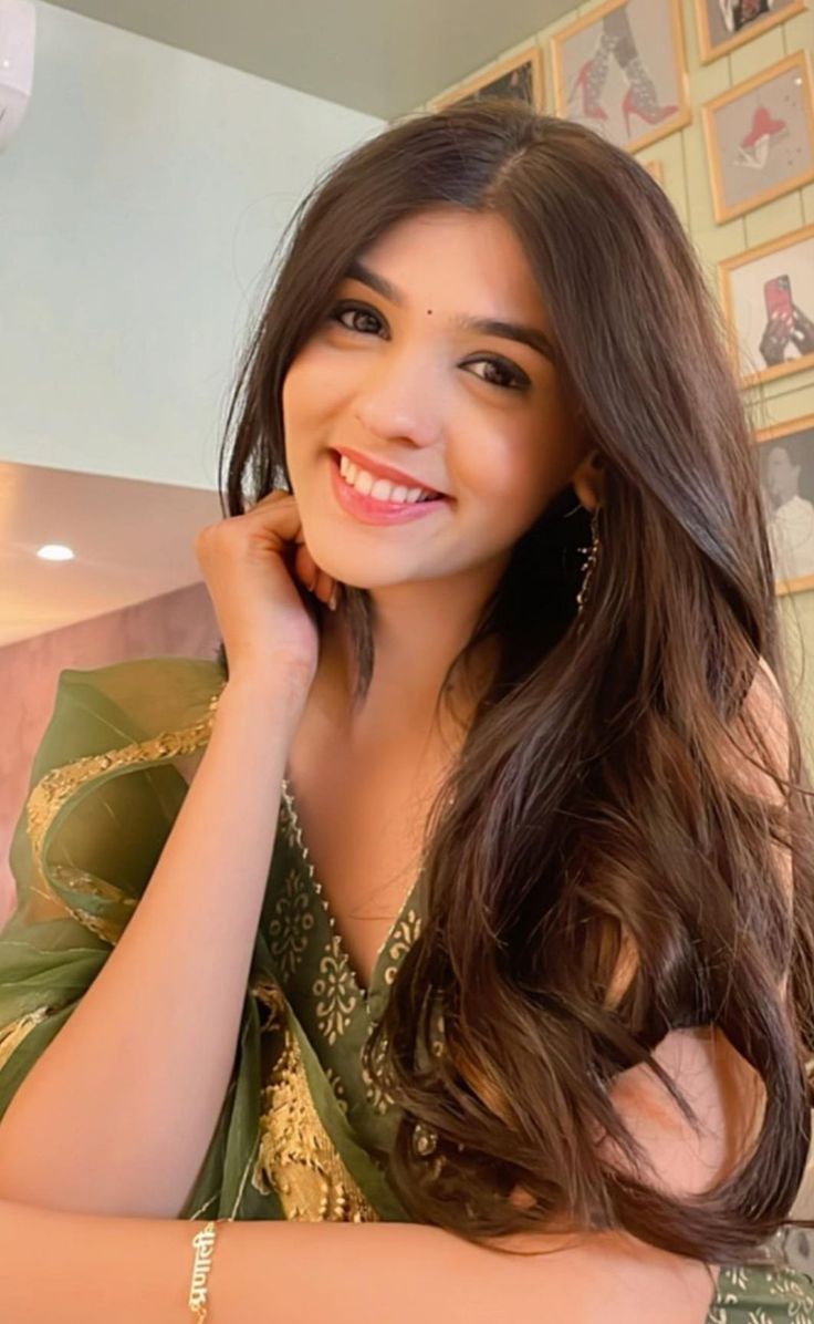 a woman with long brown hair wearing a green dress and smiling at the camera while sitting in front of a mirror