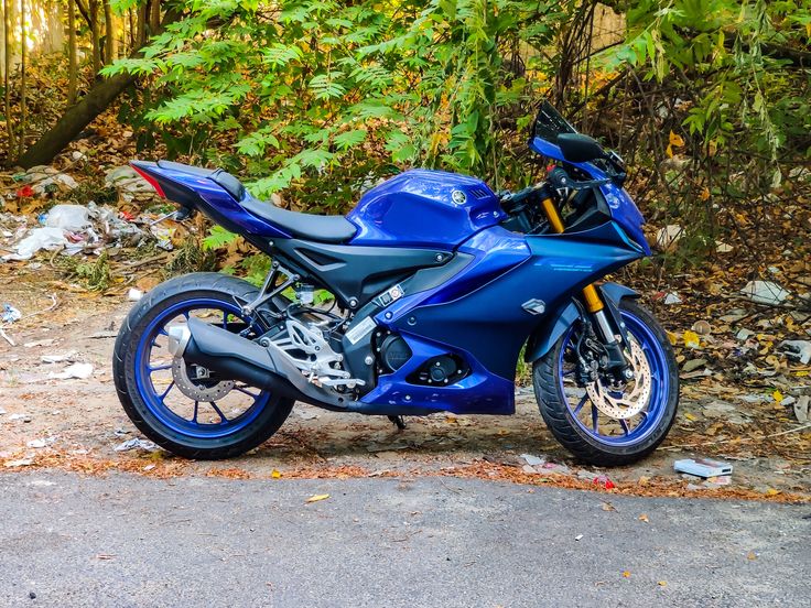 a blue motorcycle parked on the side of a road next to some trees and bushes