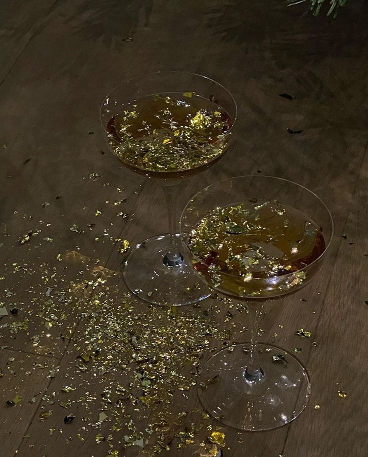 two empty wine glasses filled with food on top of a wooden table covered in confetti