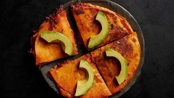 four slices of pizza with avocado cut in half on a black table top