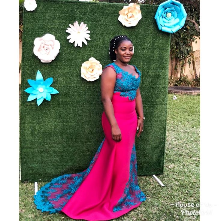 a woman in a pink and blue dress standing next to a green wall with flowers on it