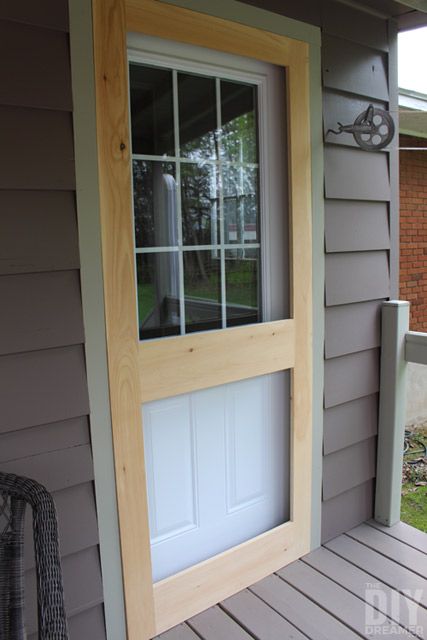 an open door on the side of a gray house with wood trim and glass panes