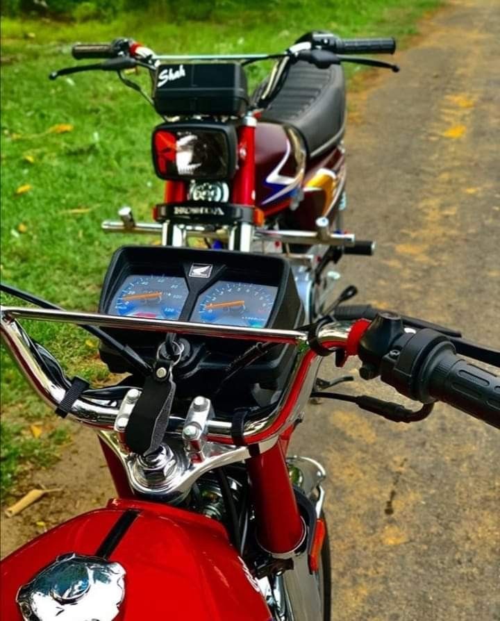 a red motorcycle parked on the side of a road next to a lush green field