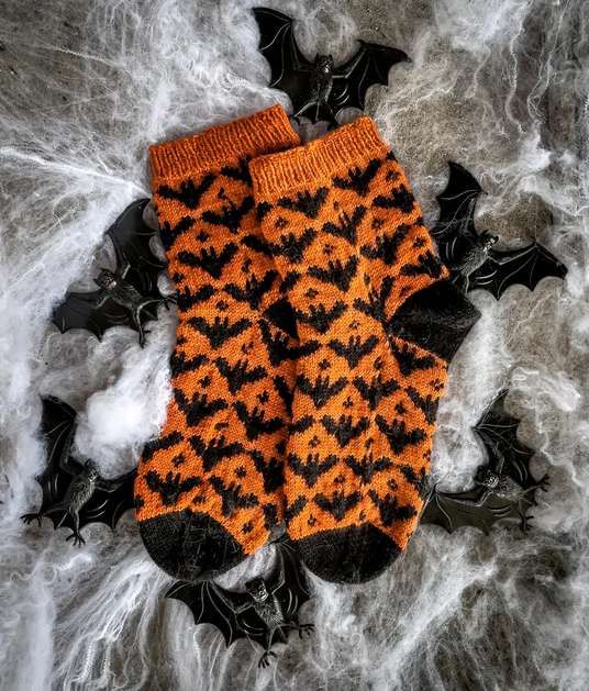 an orange and black knitted bat mitt laying on top of some white yarn