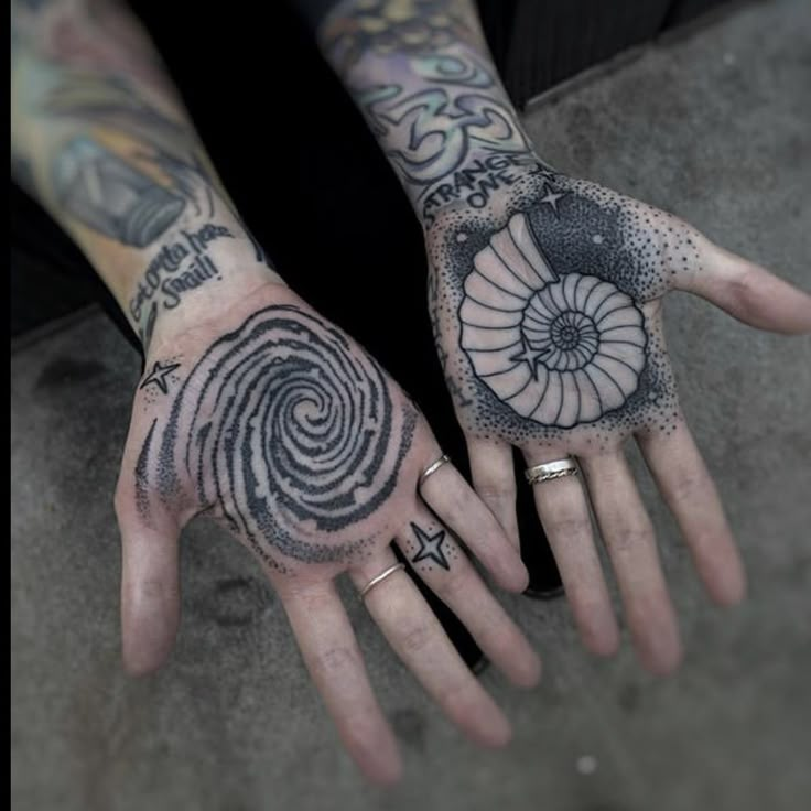 two hands with tattoos on them and one has a spiral design on the middle finger