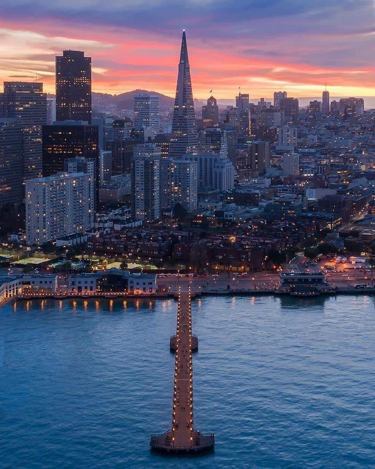 an aerial view of the city skyline at night with lights on and water in foreground