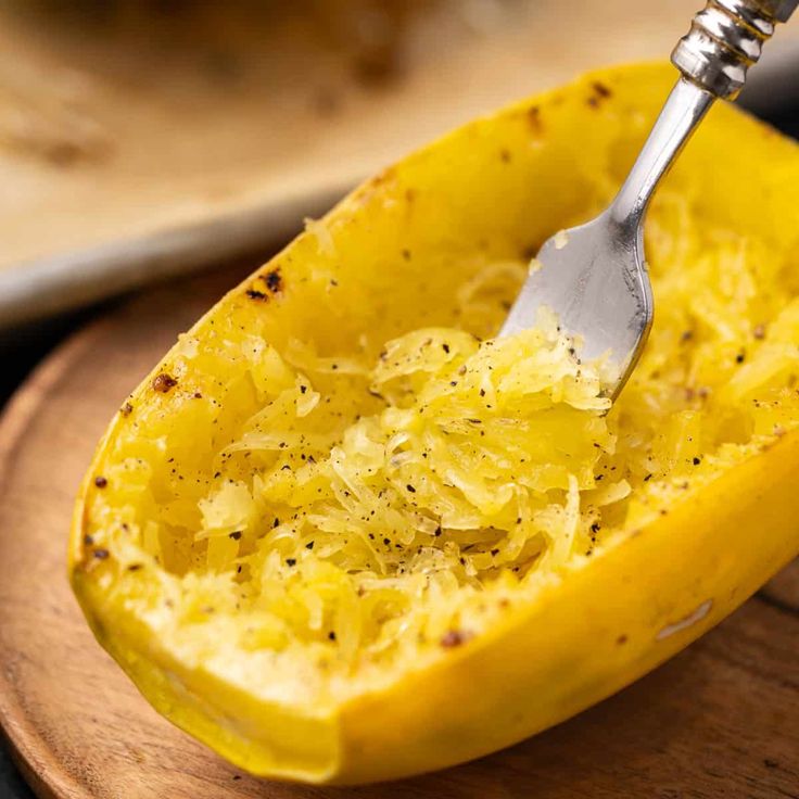 a fork in a yellow squash that is on a wooden plate with other food items