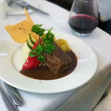 a white plate topped with meat and vegetables next to a glass of wine on a table