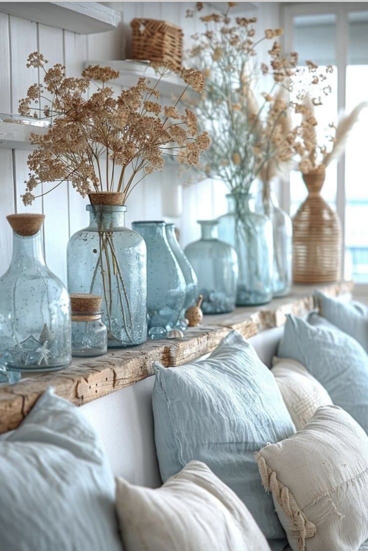 vases filled with dried flowers sit on a shelf in front of pillows and pillows