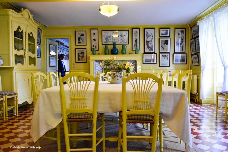 a dining room table with yellow chairs and pictures on the wall above it, in front of a checkered floor