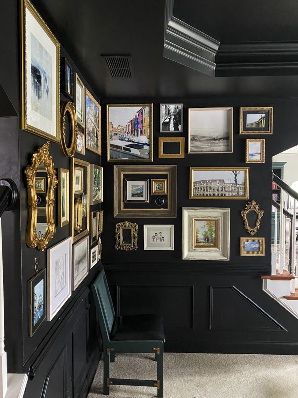 a room with black walls covered in pictures and gold framed frames on the wall, along with a green chair